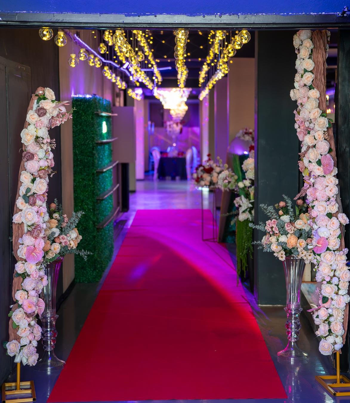 Eingang zum Hochzeitssaal mit rotem Teppich, Blumensäulen und Lichterkugeln